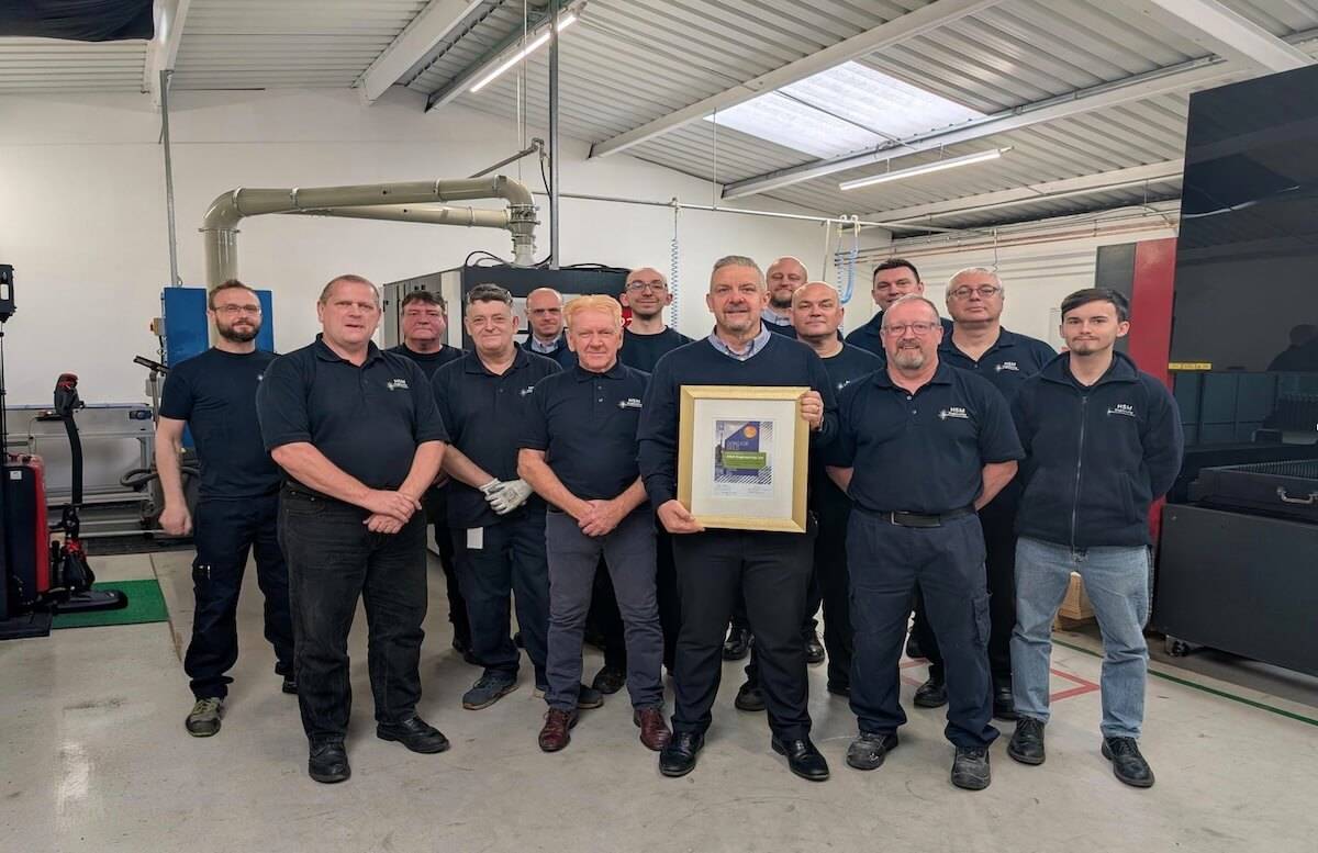 Group of manufacturing employees standing together in a factory workshop, with a manager holding an award certificate to celebrate a company achievement.